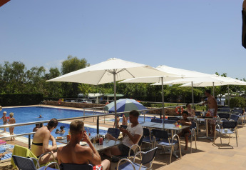 Alojamiento glamping con piscina, gente relajándose bajo sombrillas y niños jugando en el agua.