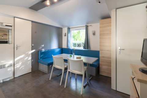 Salon de mobil-home moderne avec banquette bleue, table et chaises chez Camping del Mar, Espagne.