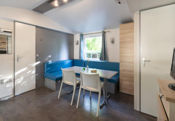 Acogedora sala de mobil home con sofá azul, mesa de comedor y sillas en Camping del Mar, España.