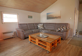 Lys stue i Holiday home «in Hünning», Tyskland, med grå hjørnesofa og pallebord med glasplade.