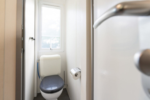Baño en una casa móvil en Camping del Mar en España, visto desde la puerta con ventana y papel higiénico.