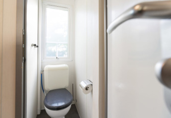 Toilettes d’un mobil-home au Camping del Mar en Espagne, vues depuis la porte avec fenêtre et papier toilette.