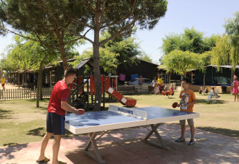 Twee mensen spelen buiten tafeltennis bij Camping del Mar MOBILE HOME 6P in Spanje, omringd door bomen.