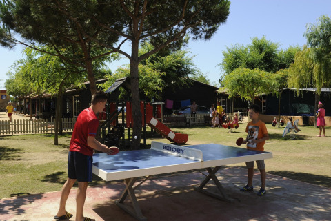 Dos personas juegan tenis de mesa al aire libre en Camping del Mar MOBILE HOME 6P en España, entre árboles.