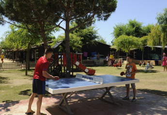 Dos personas juegan tenis de mesa al aire libre en Camping del Mar MOBILE HOME 6P en España, entre árboles.