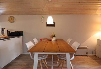 Zona pranzo in un lodge con soffitto in legno, tavolo moderno e sedie bianche a Hünning, Germania.