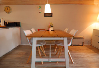 Zona pranzo nella casa vacanze «in Hünning», Germania, con tavolo in legno, sedie bianche e luce calda.