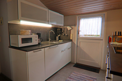 Cucina moderna in casa vacanze a Hünning, Germania, con microonde, lavello e mobili bianchi.