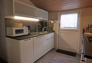 Moderne keuken in een vakantiewoning in Hünning, Duitsland, met magnetron, spoelbak en witte kasten.