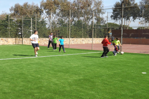 Kinder und Erwachsene spielen Fußball auf einem grünen Feld bei einer Glamping-Unterkunft im Freien.