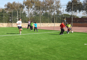 Niños y adultos juegan al fútbol en un campo verde durante una estancia de glamping bajo un cielo soleado.