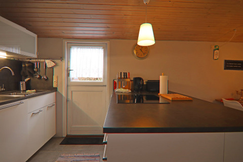 Cocina moderna en Holiday home «in Hünning», Alemania, con armarios blancos y techo de madera.