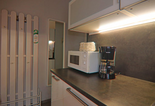 Kitchen space with coffee maker, microwave, and plates under cabinet lighting in a holiday home in Hünning.