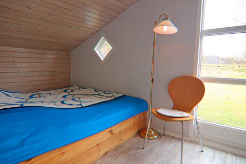 Camera accogliente con soffitto inclinato in legno, letto blu, sedia e lampada da terra in una casa vacanze a Hünning, Germania.