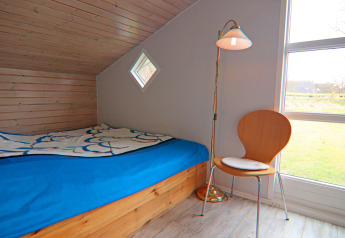 Camera accogliente con soffitto inclinato in legno, letto blu, sedia e lampada da terra in una casa vacanze a Hünning, Germania.