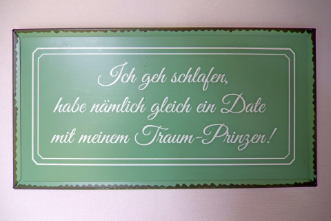 Groen metalen bord met Duitse tekst over slapen en een droomprins, gefotografeerd in een lodge in Duitsland.