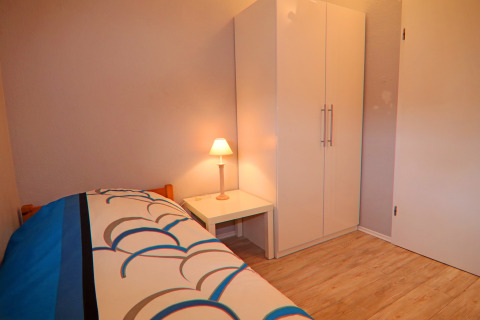 Eenvoudige slaapkamer met eenpersoonsbed, nachtlampje en witte kast bij Holiday home in Hünning, Duitsland.