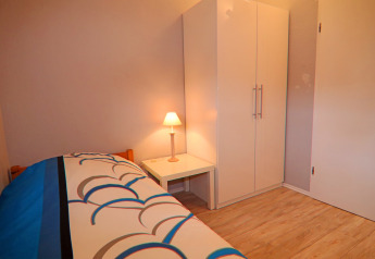 Un dormitorio sencillo con cama individual, lámpara de noche y armario blanco en Holiday home en Hünning, Alemania.