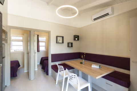 Modernes Esszimmer mit Holztisch, lila Eckbank und weißen Stühlen im Camping del Mar BUNGALOW PREMIUM, Spanien.