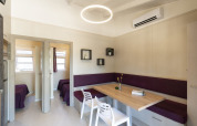 Comedor moderno con mesa de madera, banco esquinero púrpura y sillas blancas en Camping del Mar BUNGALOW PREMIUM, España.