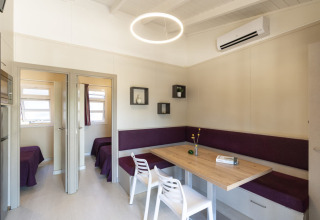 Modernes Esszimmer mit Holztisch, lila Eckbank und weißen Stühlen im Camping del Mar BUNGALOW PREMIUM, Spanien.