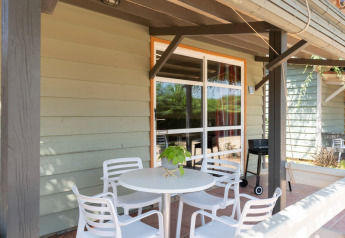Terraza exterior en Camping del Mar BUNGALOW PREMIUM en España, con mesa blanca, sillas y barbacoa.