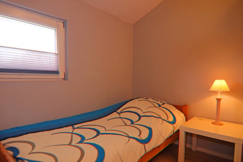A cozy bedroom with single bed, colorful duvet, bedside table and lamp at Holiday home in Hünning, Germany.