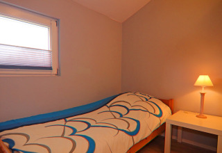 A cozy bedroom with single bed, colorful duvet, bedside table and lamp at Holiday home in Hünning, Germany.