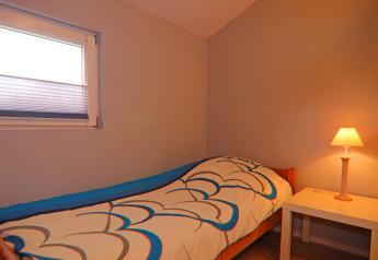 Camera accogliente con letto singolo, piumone colorato, comodino e lampada presso Holiday home a Hünning, Germania.