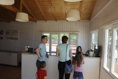 Familie checkt an der Rezeption der Camping del Mar BUNGALOW PREMIUM Lodge in Spanien ein, moderne Holzausstattung.