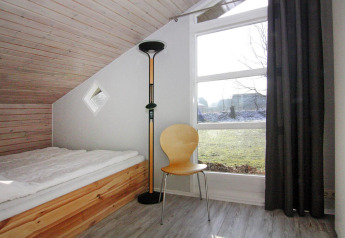 Chambre lumineuse à Holiday home «in Hünning», Allemagne, avec lit simple, chaise et grande fenêtre.