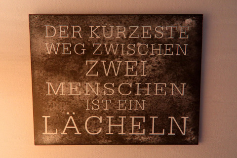 Vægskilt på et tysk lodge med citatet 'Der kürzeste Weg zwischen zwei Menschen ist ein Lächeln.'