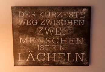 Placa mural en casa rural alemana con la frase: 'Der kürzeste Weg zwischen zwei Menschen ist ein Lächeln.'