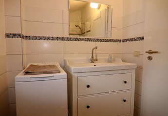 Bagno con lavandino, specchio, lavatrice e cassettiera bianca nel cottage 'in Hünning', Germania.