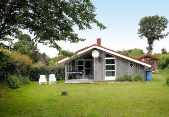 Charmante maison de vacances à Hünning, Allemagne, entourée de verdure, arbres et deux transats blancs.