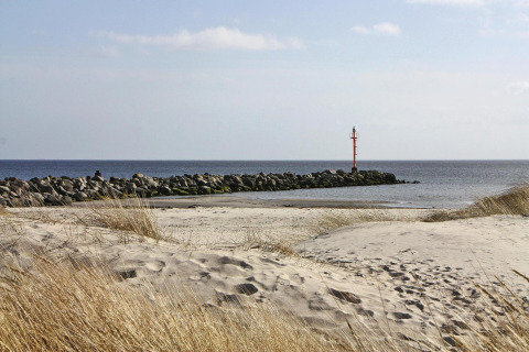 Udsigt til sandstrand, marehalm og en mole med rød fyr ved havet nær Holiday home «in Hünning», Tyskland.