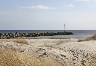 Udsigt til sandstrand, marehalm og en mole med rød fyr ved havet nær Holiday home «in Hünning», Tyskland.
