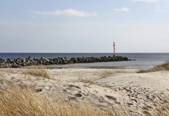Spiaggia sabbiosa, erba e un molo con segnale rosso vicino Holiday home «in Hünning», Germania.