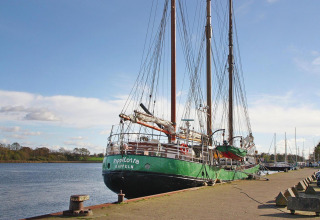 Sailing ship moored at the dock in Hünning, Germany, on a clear day with blue sky and green fields.