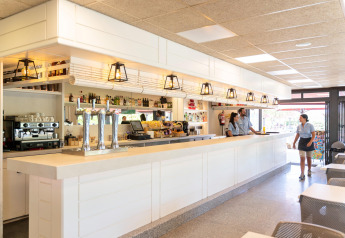 Bar moderno y luminoso en Camping del Mar BUNGALOW PREMIUM en España con personal uniformado atendiendo.