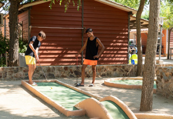 Dos jóvenes juegan al minigolf al aire libre frente a un bungalow de madera en Camping del Mar BUNGALOW PREMIUM, España.