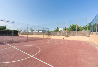 Cancha de baloncesto al aire libre en Camping del Mar BUNGALOW PREMIUM en España con suelo rojo y vallas.