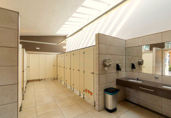 Modernes öffentliches Badezimmer mit Kabinen, Waschbecken und Spiegel im Camping del Mar Bungalow Premium in Spanien.