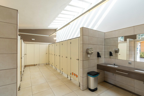 Modernes öffentliches Badezimmer mit Kabinen, Waschbecken und Spiegel im Camping del Mar Bungalow Premium in Spanien.