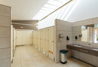 Modernes öffentliches Badezimmer mit Kabinen, Waschbecken und Spiegel im Camping del Mar Bungalow Premium in Spanien.