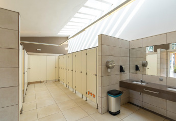 Baño público moderno con cabinas, lavabos y luz natural en Camping del Mar Bungalow Premium en España.