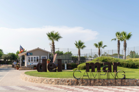 Eingang zum Camping del Mar BUNGALOW PREMIUM in Spanien mit Palmen, Schild und Rezeption im Freien.