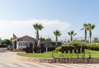 Eingang zum Camping del Mar BUNGALOW PREMIUM in Spanien mit Palmen, Schild und Rezeption im Freien.