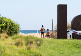 Dos personas con ropa de baño caminan hacia la playa desde Camping del Mar BUNGALOW PREMIUM en España bajo el sol.