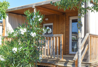 Mobilhome 'Els Pins- Mobile-Home Plus 2' i Spanien med træterrasse og blomstrende buske foran.